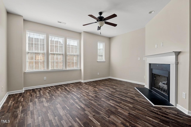 unfurnished living room with a fireplace with raised hearth, ceiling fan, visible vents, and dark wood-style floors