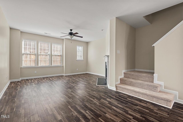 unfurnished living room featuring a ceiling fan, a fireplace, stairway, baseboards, and dark wood-style floors