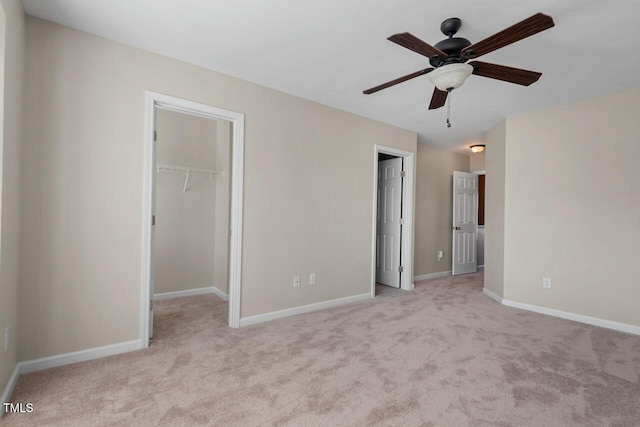 unfurnished bedroom with baseboards, a spacious closet, light carpet, and ceiling fan