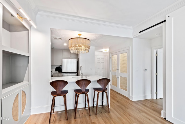 kitchen with ornamental molding, a peninsula, light countertops, freestanding refrigerator, and light wood-style floors