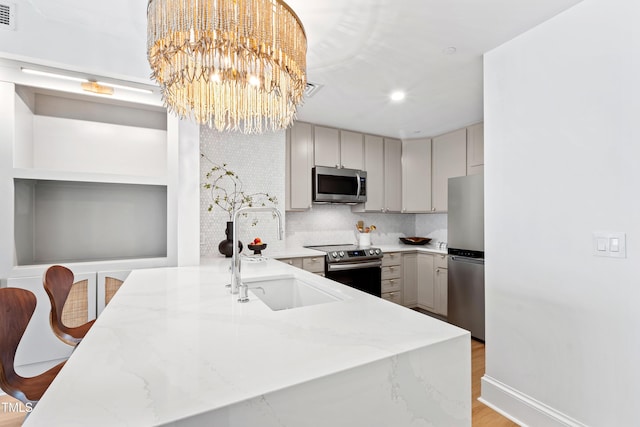 kitchen featuring a notable chandelier, a sink, gray cabinetry, light stone countertops, and stainless steel appliances