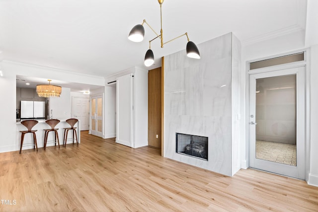 living area with light wood-style floors, a high end fireplace, a notable chandelier, and ornamental molding