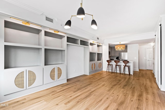 unfurnished living room featuring ornamental molding, visible vents, a notable chandelier, and wood finished floors