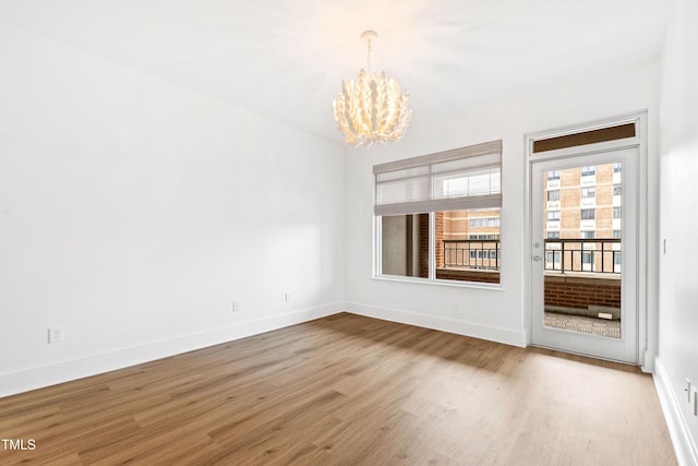 empty room with a chandelier, baseboards, and wood finished floors