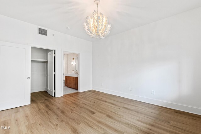 unfurnished bedroom with baseboards, light wood-type flooring, an inviting chandelier, a spacious closet, and visible vents
