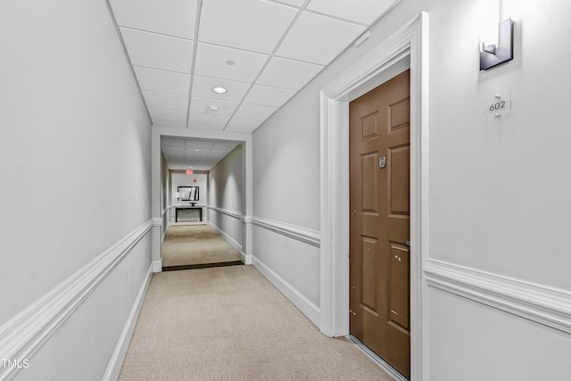 hall with light carpet, a paneled ceiling, baseboards, and wainscoting