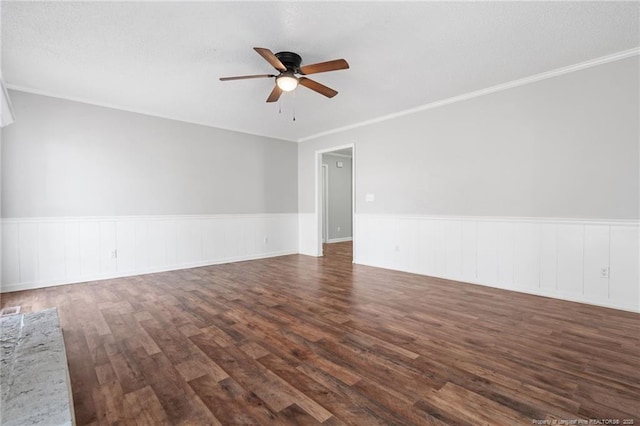 spare room with dark wood-style flooring, wainscoting, a ceiling fan, and crown molding