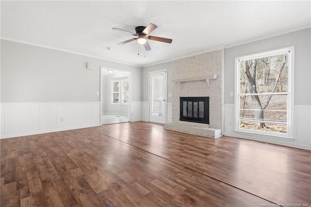 unfurnished living room with wainscoting, a textured ceiling, a ceiling fan, and wood finished floors