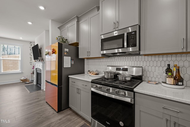 kitchen featuring tasteful backsplash, light wood-type flooring, appliances with stainless steel finishes, a fireplace, and gray cabinets