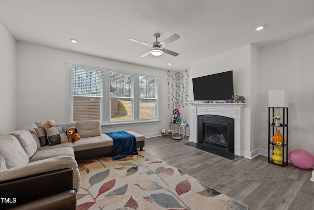 living area featuring a glass covered fireplace, baseboards, recessed lighting, a ceiling fan, and wood finished floors