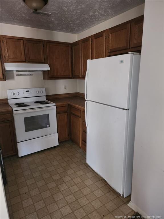 kitchen with dark countertops, under cabinet range hood, tile patterned floors, white appliances, and a textured ceiling