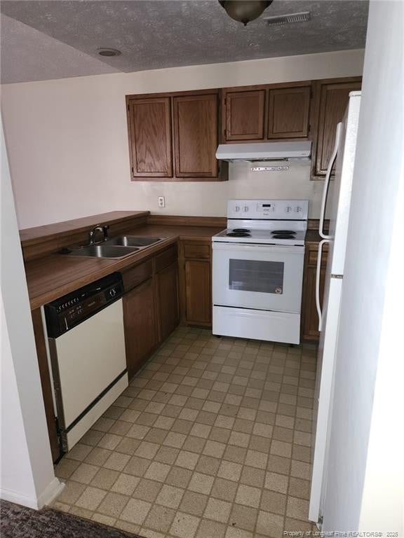 kitchen featuring white appliances, light floors, under cabinet range hood, and a sink