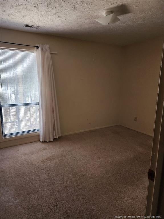 spare room featuring visible vents, light carpet, and a textured ceiling