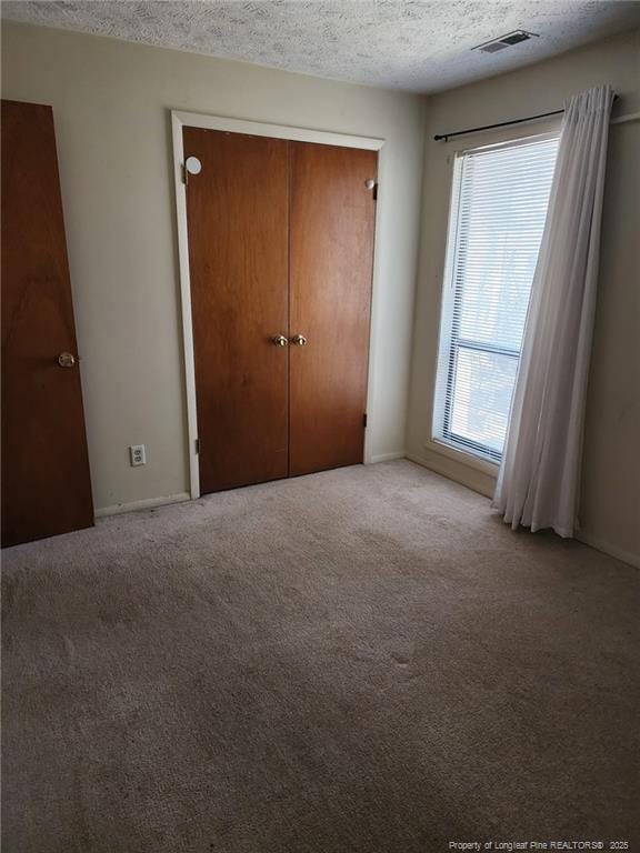 unfurnished bedroom featuring visible vents, light carpet, a textured ceiling, and a closet