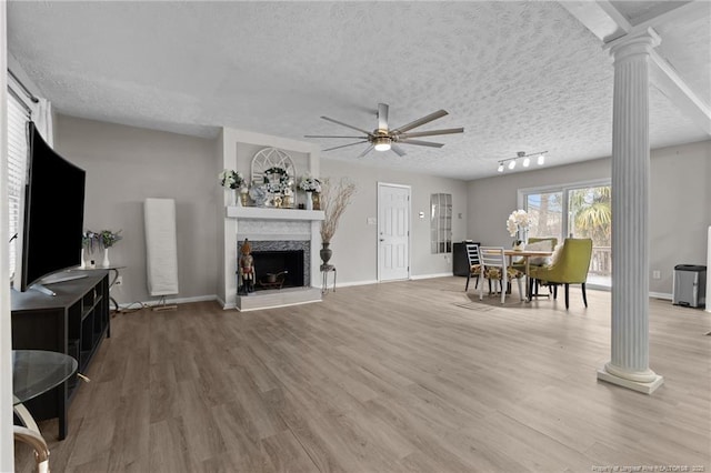 living room with a textured ceiling, a ceiling fan, ornate columns, and wood finished floors