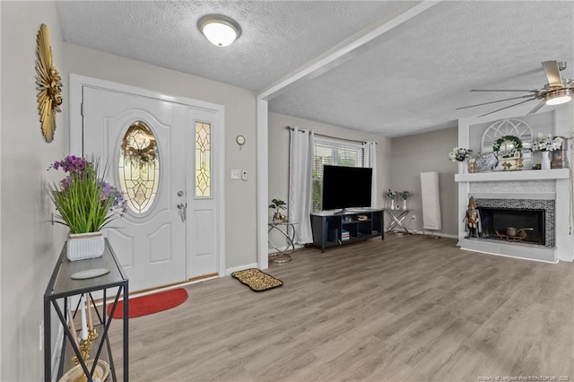 entryway featuring a ceiling fan, a textured ceiling, wood finished floors, and a fireplace with raised hearth