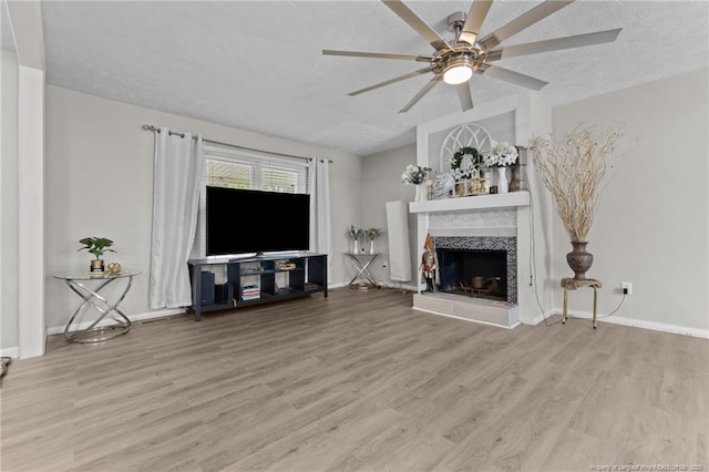 unfurnished living room with baseboards, ceiling fan, a fireplace, wood finished floors, and a textured ceiling