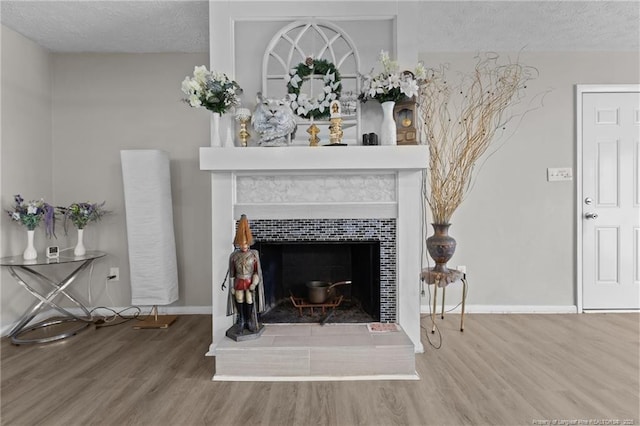 interior details with a tiled fireplace, a textured ceiling, and wood finished floors