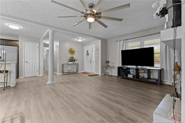 living room featuring ceiling fan, a textured ceiling, light wood-style floors, and decorative columns