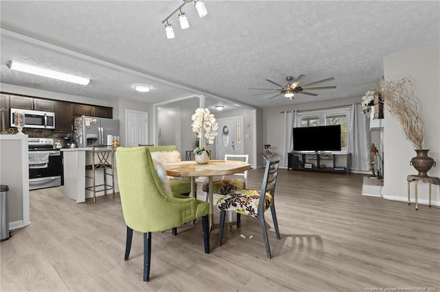 dining area featuring baseboards, light wood-style flooring, a textured ceiling, and a ceiling fan