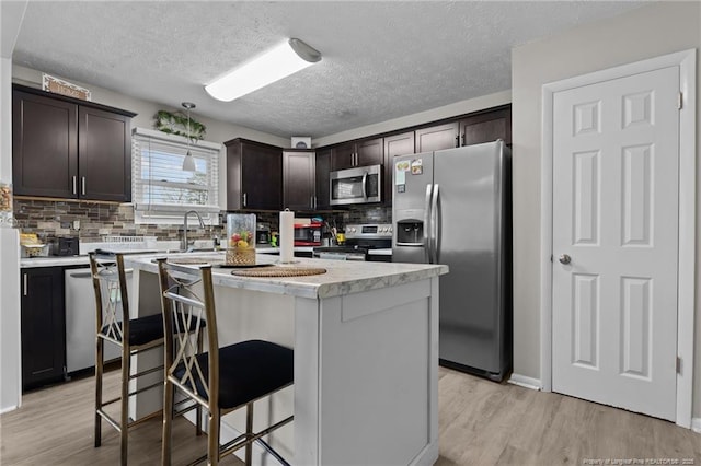 kitchen with light wood finished floors, light countertops, dark brown cabinets, appliances with stainless steel finishes, and a center island