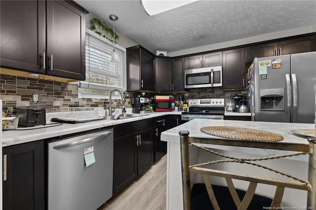 kitchen featuring a sink, light wood-style floors, appliances with stainless steel finishes, dark brown cabinetry, and decorative backsplash