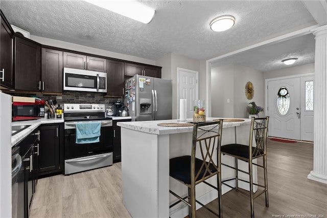 kitchen with light countertops, decorative columns, light wood-style floors, and stainless steel appliances