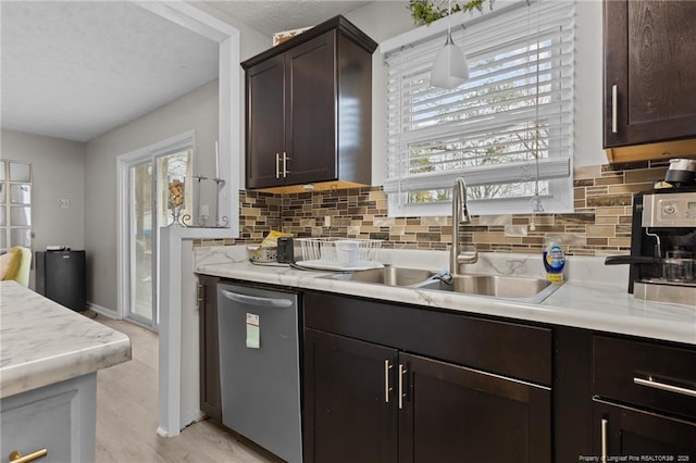 kitchen featuring backsplash, dark brown cabinetry, light countertops, stainless steel dishwasher, and a sink