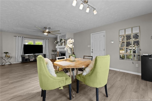 dining area with a ceiling fan, a textured ceiling, wood finished floors, a fireplace, and baseboards