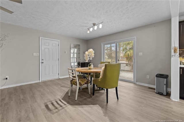 dining space with baseboards, a textured ceiling, and light wood finished floors