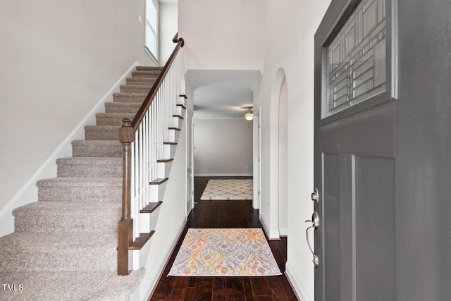 foyer featuring dark wood-type flooring, a ceiling fan, a towering ceiling, stairs, and arched walkways