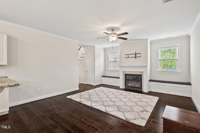 unfurnished living room featuring ornamental molding, healthy amount of natural light, dark wood-style flooring, a ceiling fan, and a glass covered fireplace