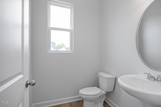 half bathroom with wood finished floors, toilet, baseboards, and a sink
