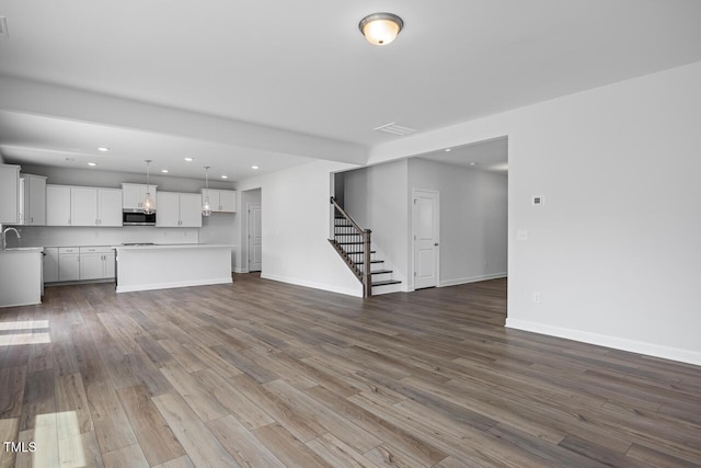 unfurnished living room featuring dark wood-style floors, stairway, baseboards, and recessed lighting