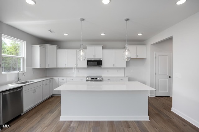 kitchen featuring stainless steel appliances, light countertops, a kitchen island, white cabinets, and a sink