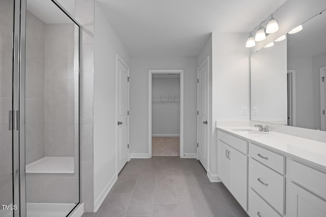 bathroom featuring tile patterned flooring, a walk in closet, vanity, baseboards, and a stall shower