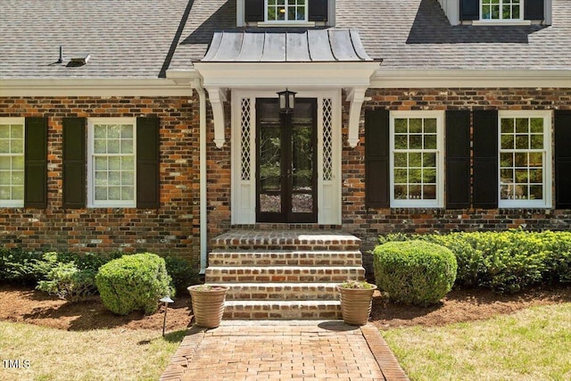 view of exterior entry with roof with shingles, brick siding, a standing seam roof, and french doors