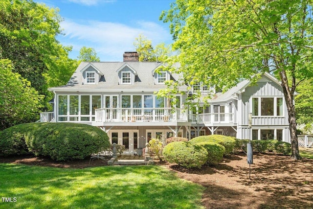 back of property featuring a sunroom, a chimney, a yard, a wooden deck, and board and batten siding