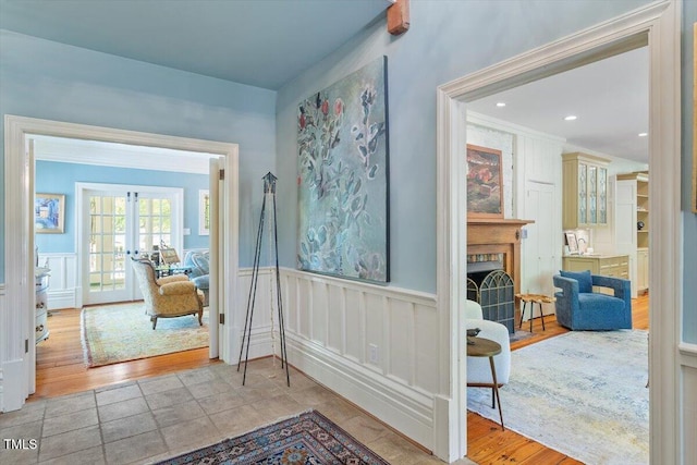 foyer entrance with french doors, a fireplace, wainscoting, wood finished floors, and a decorative wall