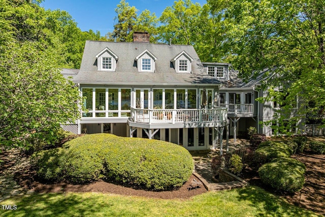 rear view of house with a wooden deck, a chimney, and a sunroom