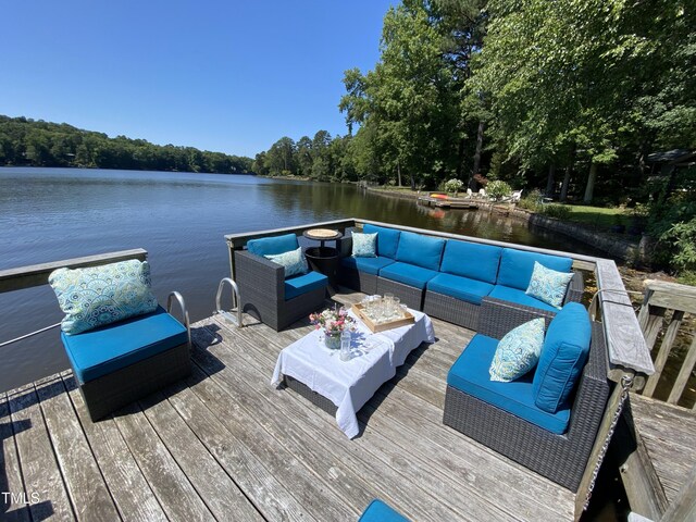 dock area with an outdoor living space, a deck with water view, and a view of trees
