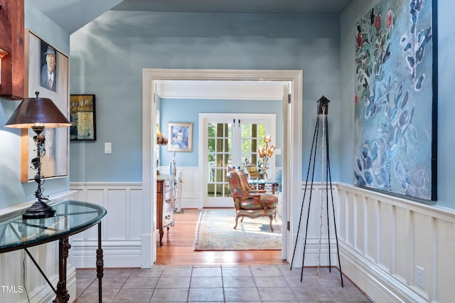 hall featuring tile patterned flooring, a wainscoted wall, and a decorative wall