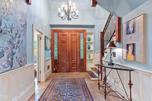foyer entrance featuring stairway, a chandelier, a decorative wall, tile patterned floors, and a wainscoted wall