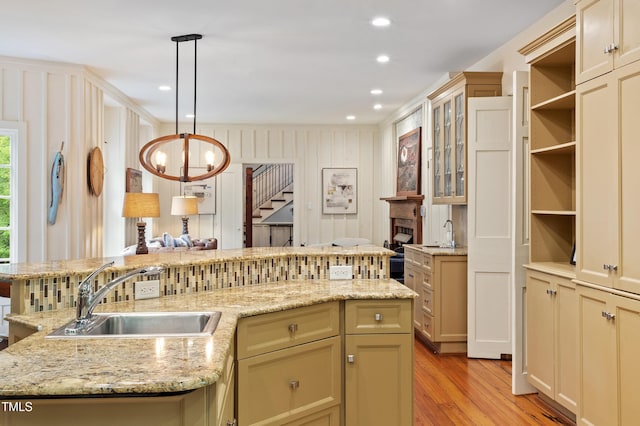 kitchen with a sink, light wood-style flooring, a chandelier, glass insert cabinets, and pendant lighting