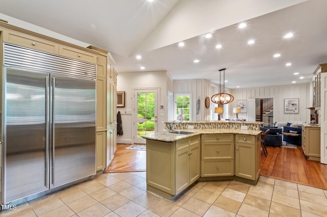 kitchen with built in fridge, open floor plan, a sink, lofted ceiling, and an island with sink