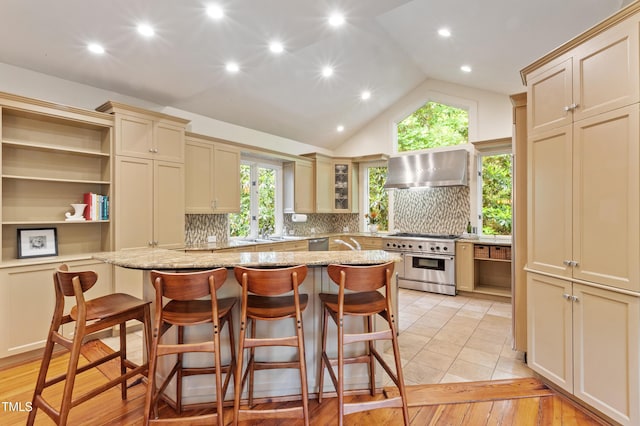 kitchen featuring stainless steel appliances, wall chimney range hood, a kitchen island, decorative backsplash, and lofted ceiling