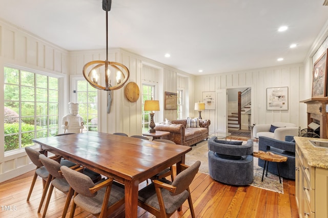 dining space featuring light wood-style floors, ornamental molding, stairway, a chandelier, and a decorative wall