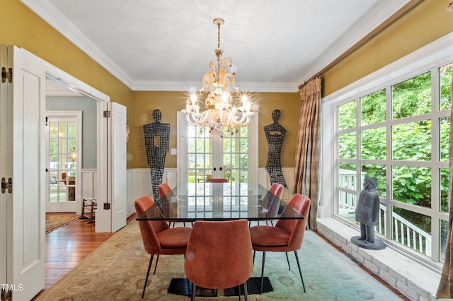 dining room with a chandelier, healthy amount of natural light, light wood-style floors, wainscoting, and a decorative wall