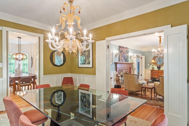 dining space featuring a chandelier, hardwood / wood-style floors, crown molding, a wainscoted wall, and a decorative wall