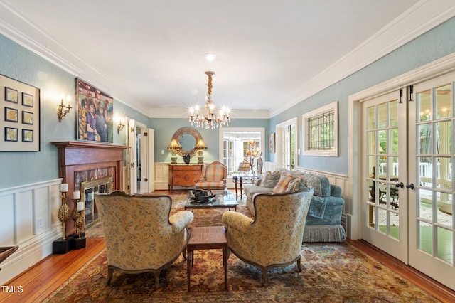 living area featuring wood-type flooring, crown molding, wainscoting, a chandelier, and a brick fireplace